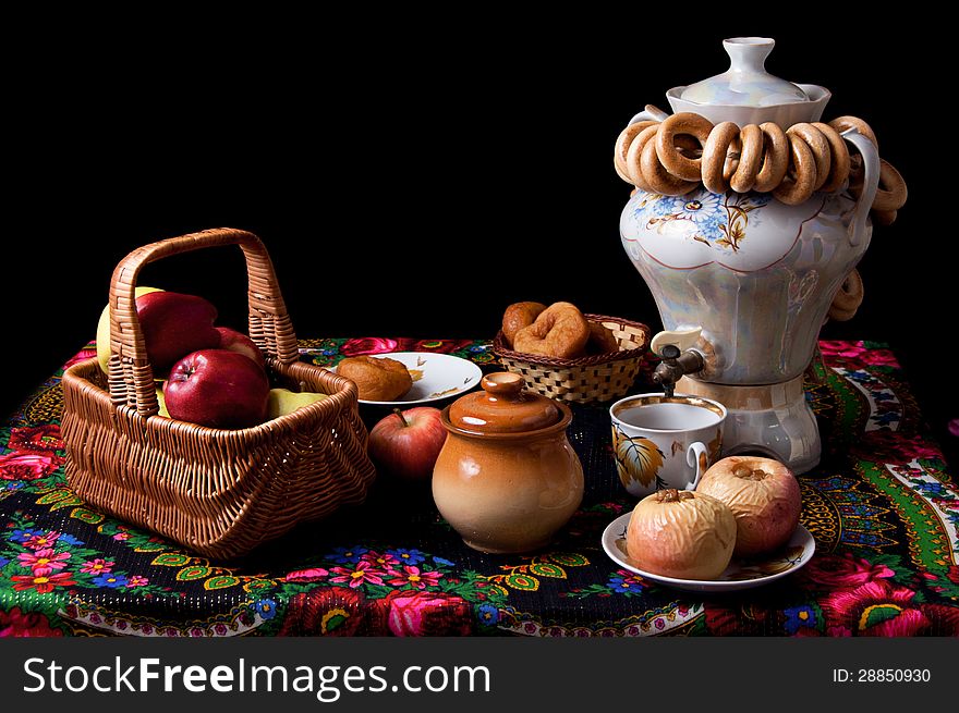 Samovar, bagels and apples on table over black