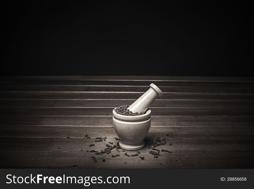 Marble mortar with spices black pepper and carnation on a wooden table