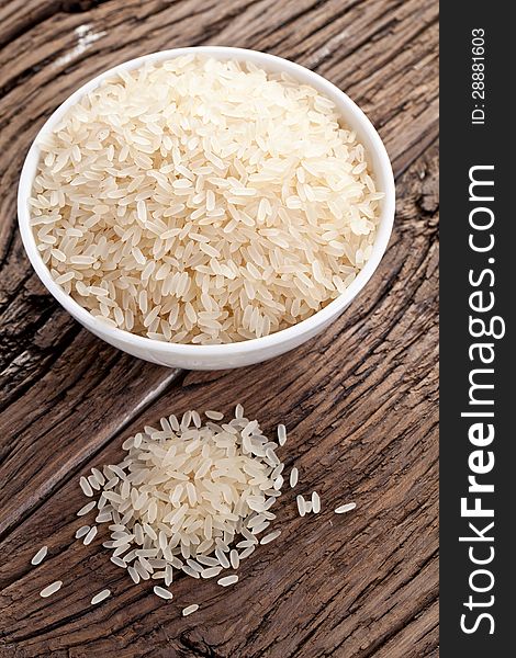 Uncooked rice in a bowl on a dark wooden table.