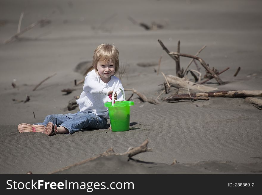 Cute blonde child playing at the beach with green bucket and pink shovel.