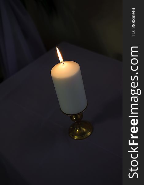 One light thick candle on a dark background with tall flame