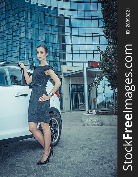 Business lady posing with a white car and skyscraper on the background