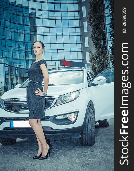 Business lady posing with a white car and skyscraper on the background