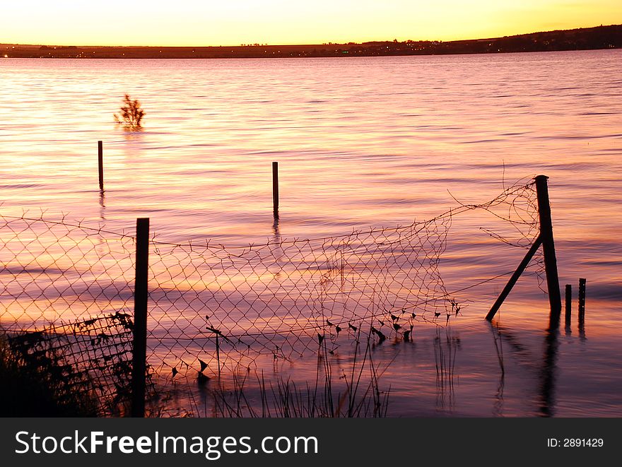 Lake sunset with a submerged crosslink fence in the foreground. Lake sunset with a submerged crosslink fence in the foreground