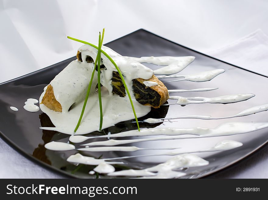 Decorated baked roll with spinach on a black plate