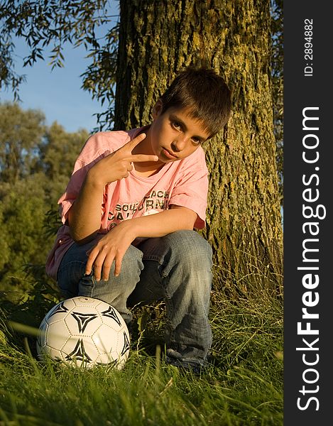 Boy shows the peacesign and holds a soccerball. Boy shows the peacesign and holds a soccerball