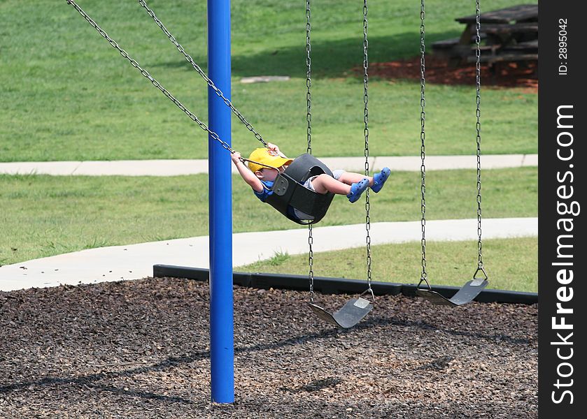 A small child wearing a cap on a park swing. A small child wearing a cap on a park swing
