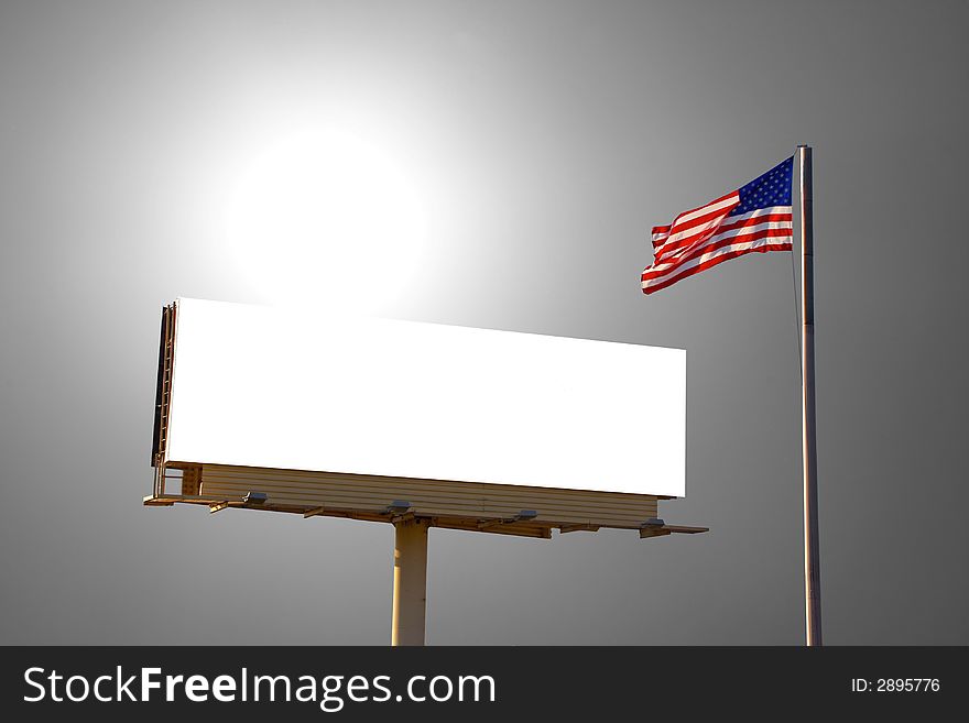 A roadside billboard with an American Flag next to it. The sun was behind the billboard and to the left. A roadside billboard with an American Flag next to it. The sun was behind the billboard and to the left