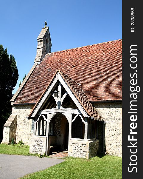 Medieval English Church with Bell Tower and carved wooden entrance Porch against a clear blue Summer Sky