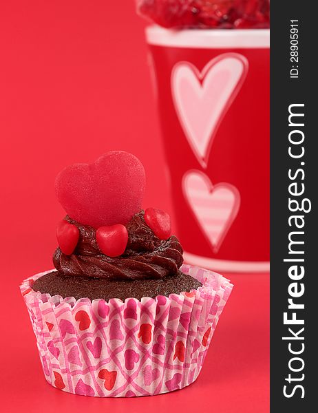 Moist chocolate cupcake with an icing swirl topped with candy hearts on red background. Moist chocolate cupcake with an icing swirl topped with candy hearts on red background