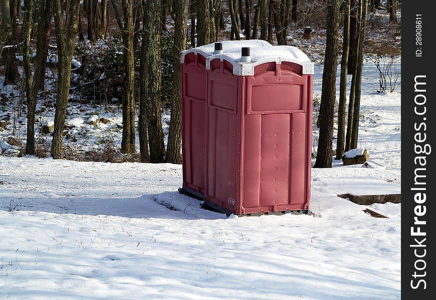 A pair of red outhouses sit in snow in a wintry forest. A pair of red outhouses sit in snow in a wintry forest.