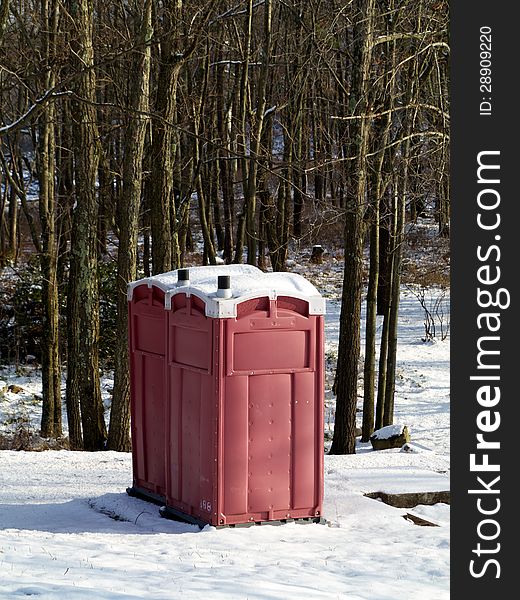 A pair of red outhouses sit in snow in a wintry forest. A pair of red outhouses sit in snow in a wintry forest.