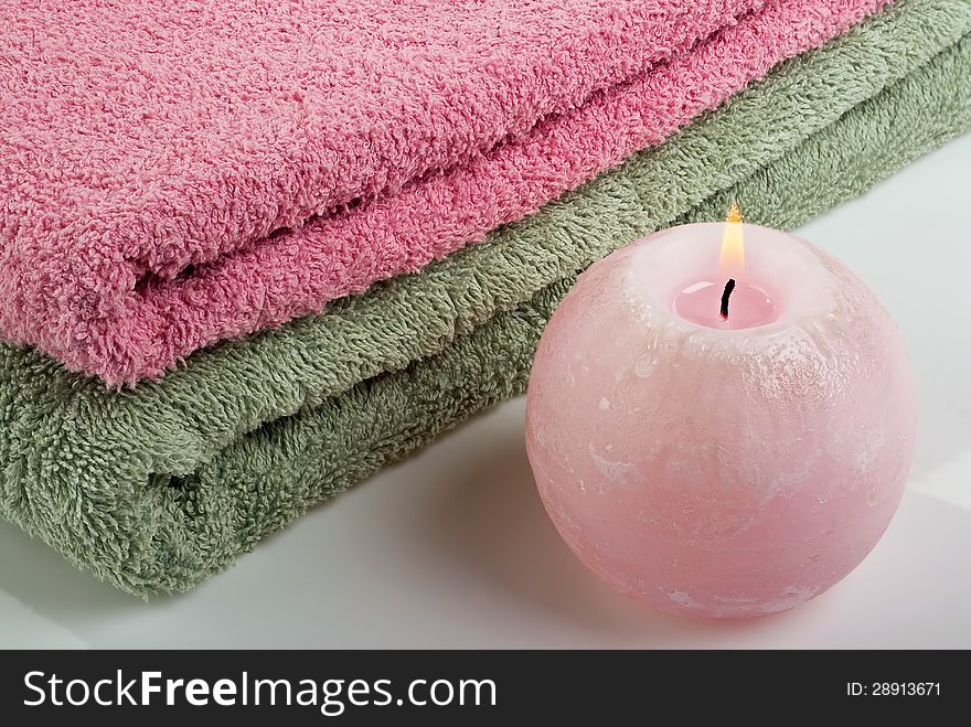 Aromatic candle and two colored towels on a white background.