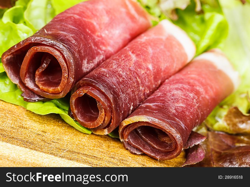 Slices of prosciutto rolled up and arranged on a lettuce leaf.