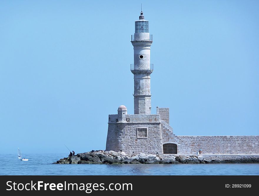 View of the lighthouse and a man fishing at the entrance to the harbor at Chania, Crete, Greece. View of the lighthouse and a man fishing at the entrance to the harbor at Chania, Crete, Greece.
