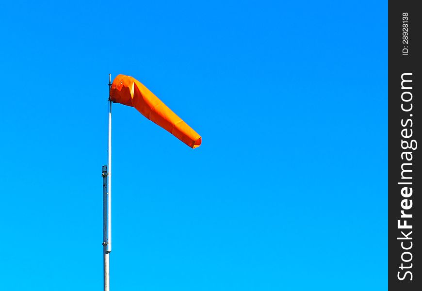 Orange windsock to measure wind blowing on a clear blue sky day.