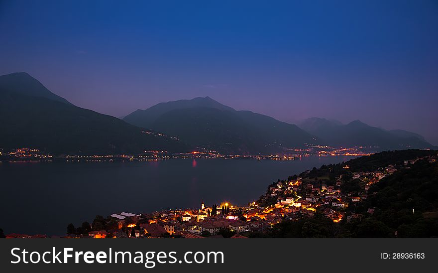Misty evening panorama Lake Como with shining lights along the shore.