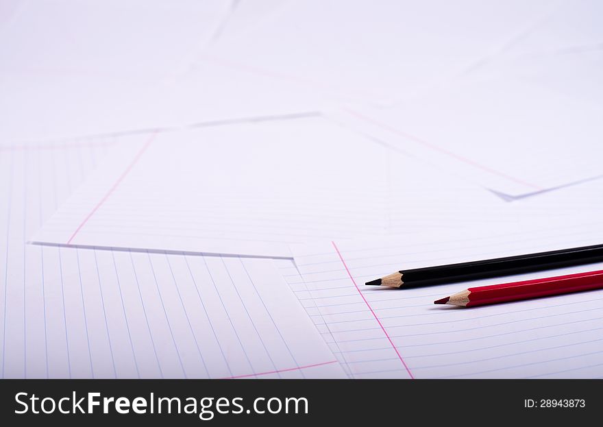 Black and red pencil exactly lie on a surface from writing-book sheets