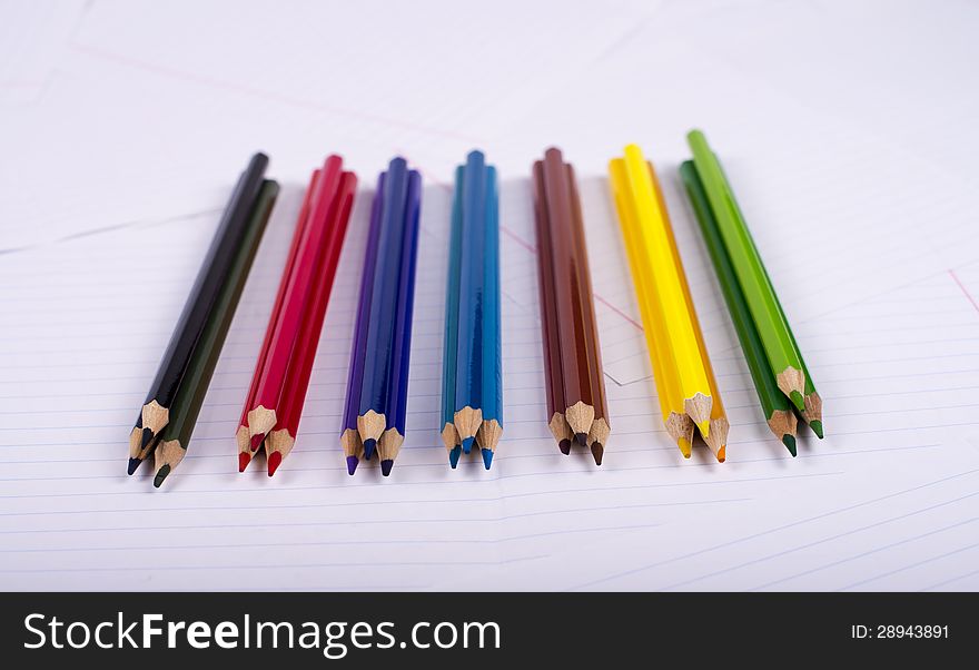 Color pencils lie small groups on three pieces on a surface from writing-book sheets