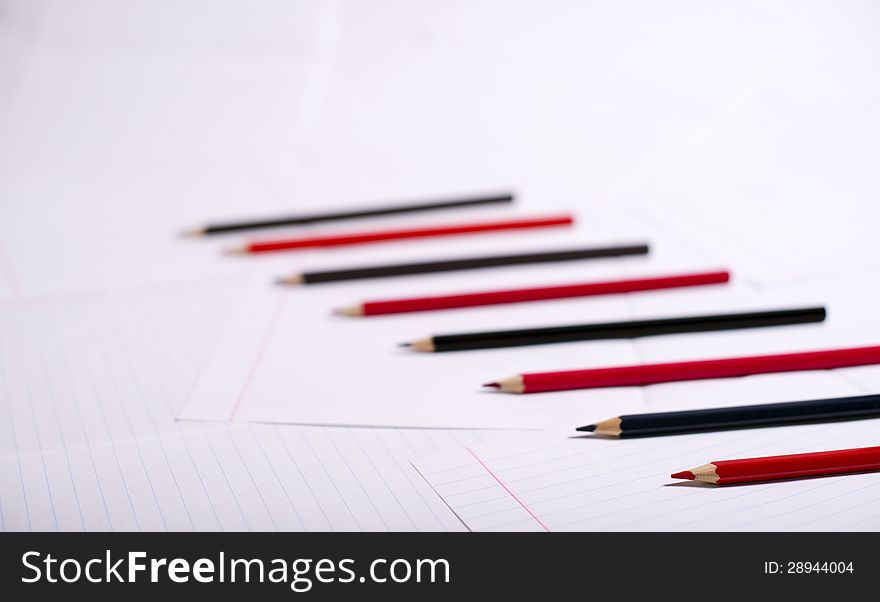 Black and red pencils lie exactly serially on a surface from writing-book sheets