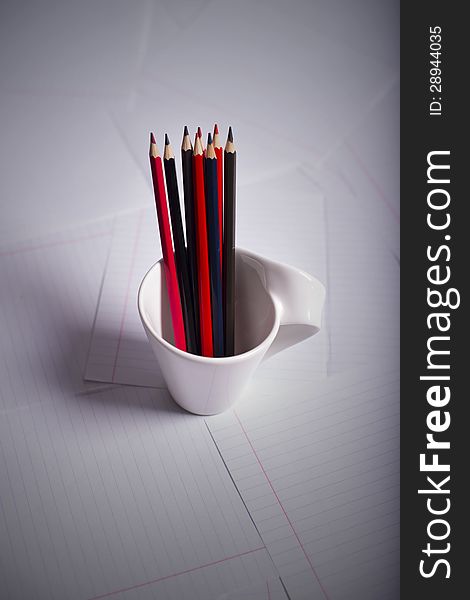 Black and red pencils stand in a white mug