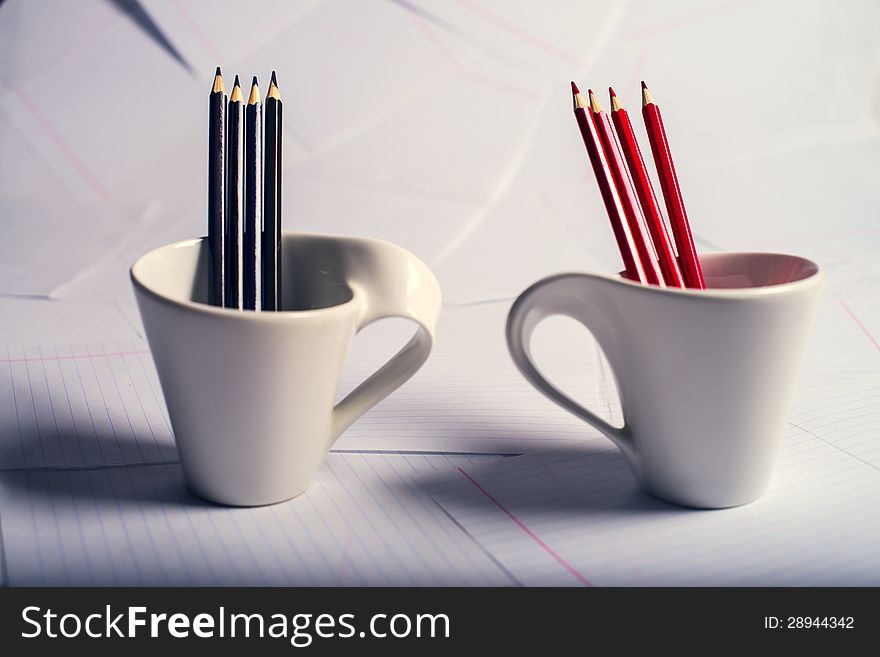 Black and red pencils stand in two white cups