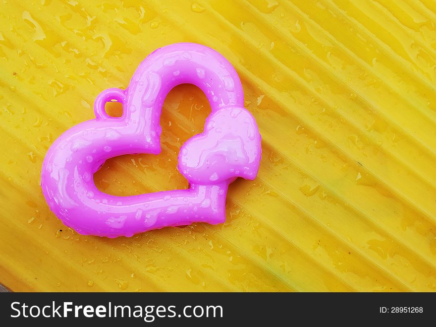 Pink heart on yellow banana leaf background. Pink heart on yellow banana leaf background