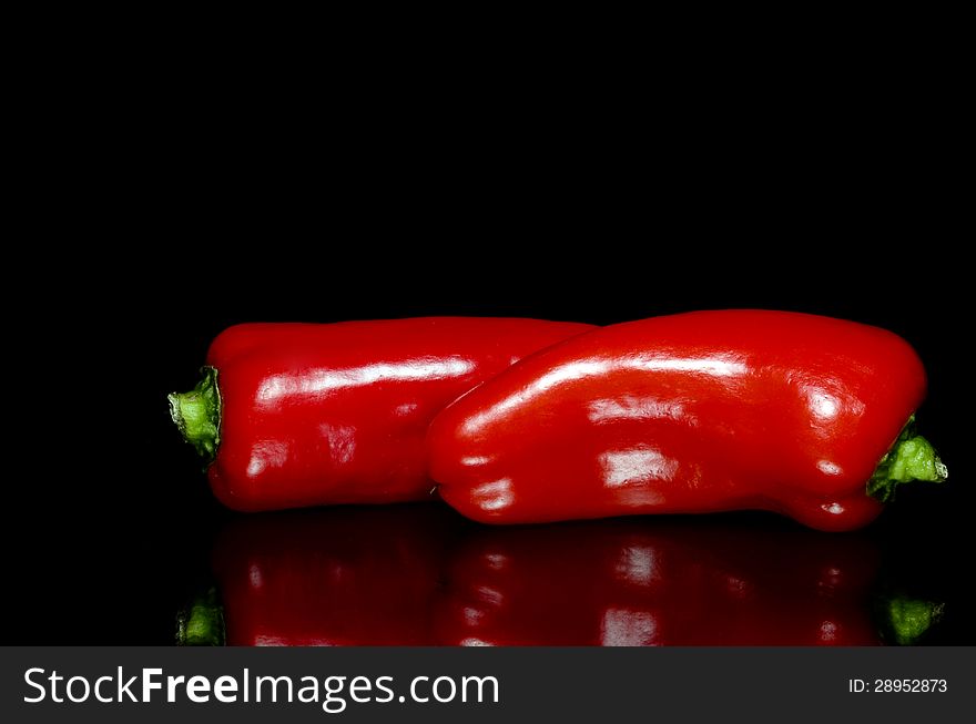 Two red peppers on black background with reflection