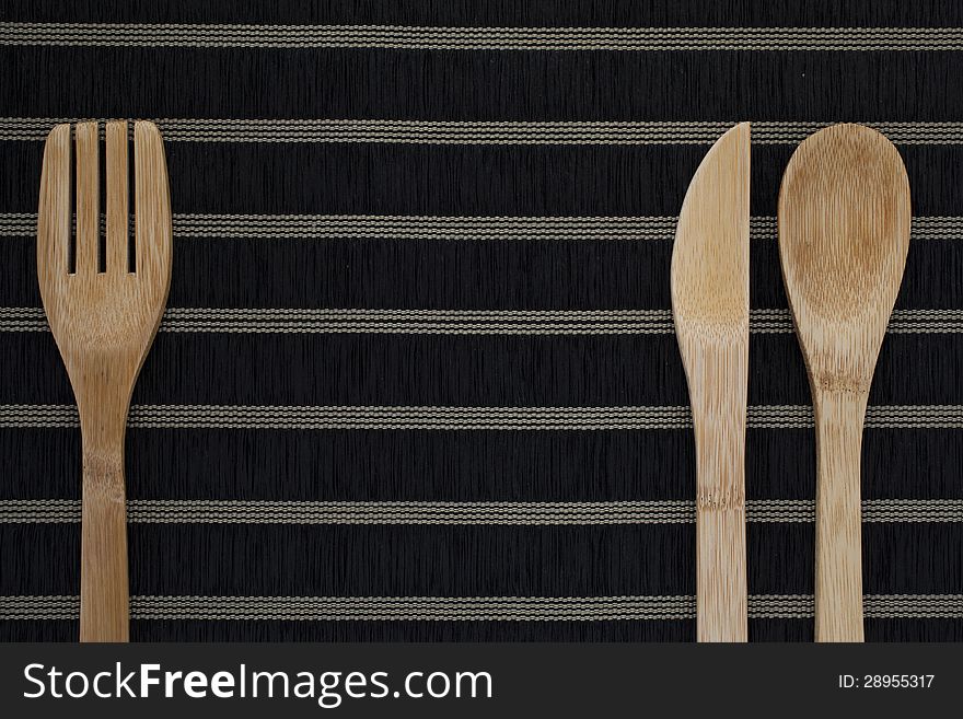 Wooden eating utensils:fork,knife and spoon on black background with horizontal stripes. Wooden eating utensils:fork,knife and spoon on black background with horizontal stripes