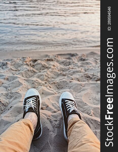 First-person View Of Men& X27 S Feet In Sneakers On Beach Against Backdrop Of Sea. Vacation, Summer Vacation Concept.