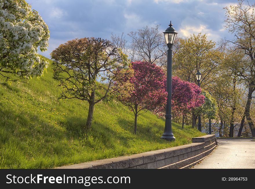 Lamps and trees on a hill next to a sidewalk under a cloudy sky. Lamps and trees on a hill next to a sidewalk under a cloudy sky