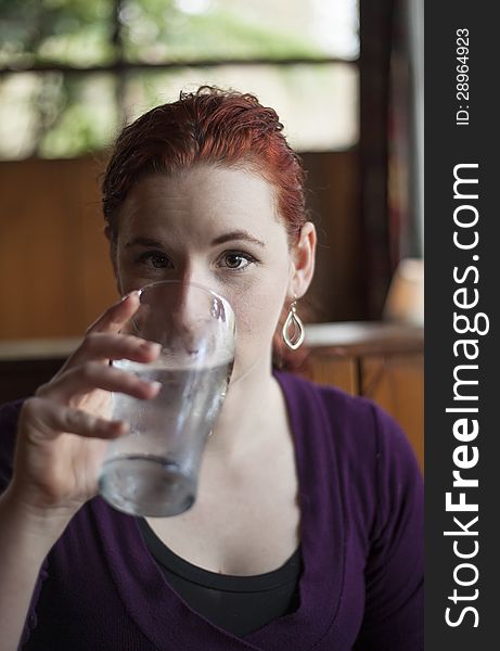 Beautiful young woman with red hair drinking water with ice from a pint glass. Beautiful young woman with red hair drinking water with ice from a pint glass.