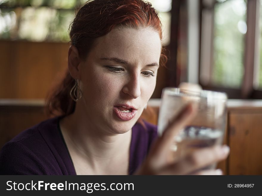 Beautiful young woman with red hair drinking water with ice from a pint glass. Beautiful young woman with red hair drinking water with ice from a pint glass.