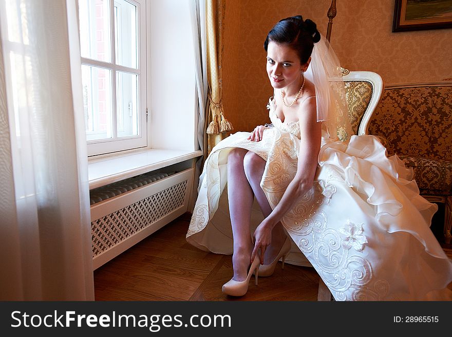 Happy bride wears her shoes and looking at camera