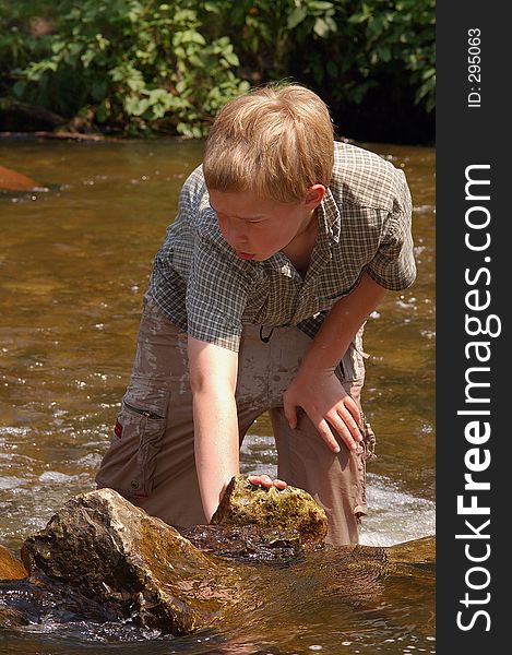 A boy plays in a creek fully dressed on a hot summer day. A boy plays in a creek fully dressed on a hot summer day