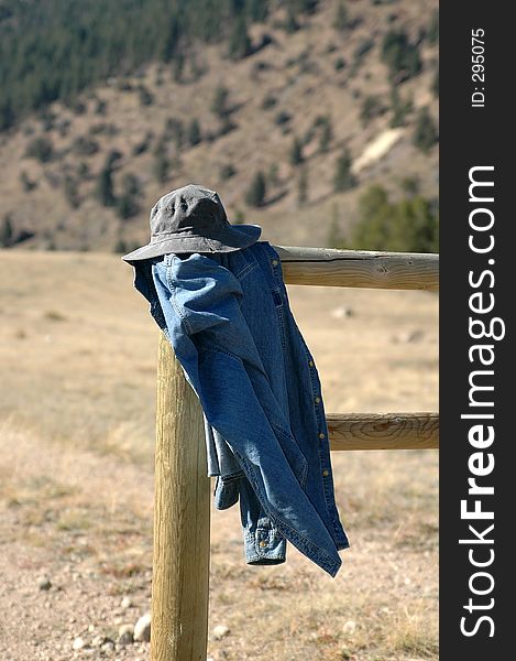 Coat and hat have been left on a fence post in the mountains. Coat and hat have been left on a fence post in the mountains