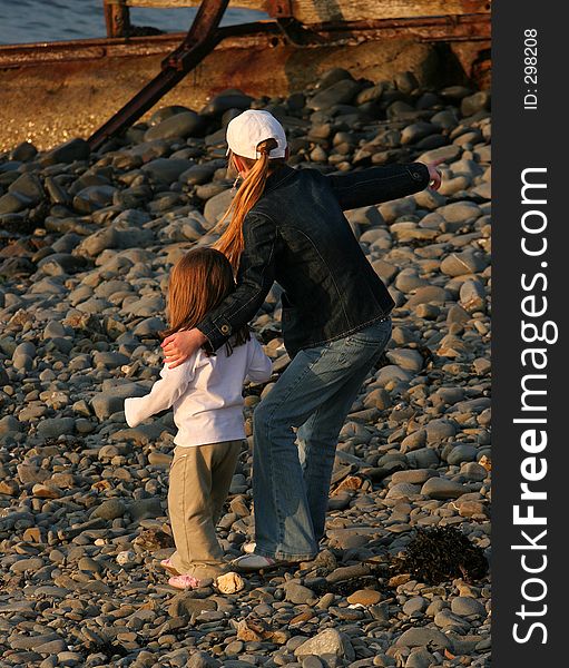 A young girl with her arm protectively around a younger child, standing on a pebble beach. A young girl with her arm protectively around a younger child, standing on a pebble beach.