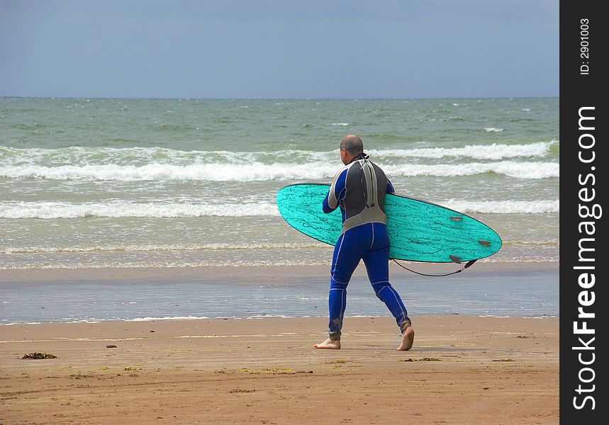 Beach scene of a man carrying a surf board, walking towards the sea. Beach scene of a man carrying a surf board, walking towards the sea