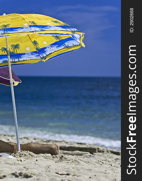 Man resting under a big colorful umbrella on a sunny beach