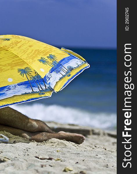 Man resting under a big colorful umbrella on a sunny beach