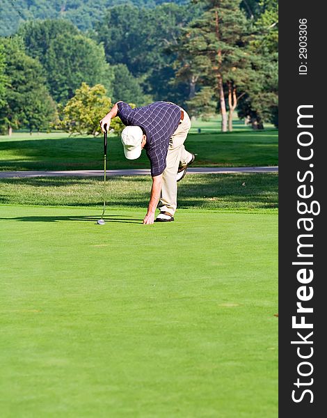 A male golfer bends to retrieve his ball from the hole. Space for copy in foreground. A male golfer bends to retrieve his ball from the hole. Space for copy in foreground.