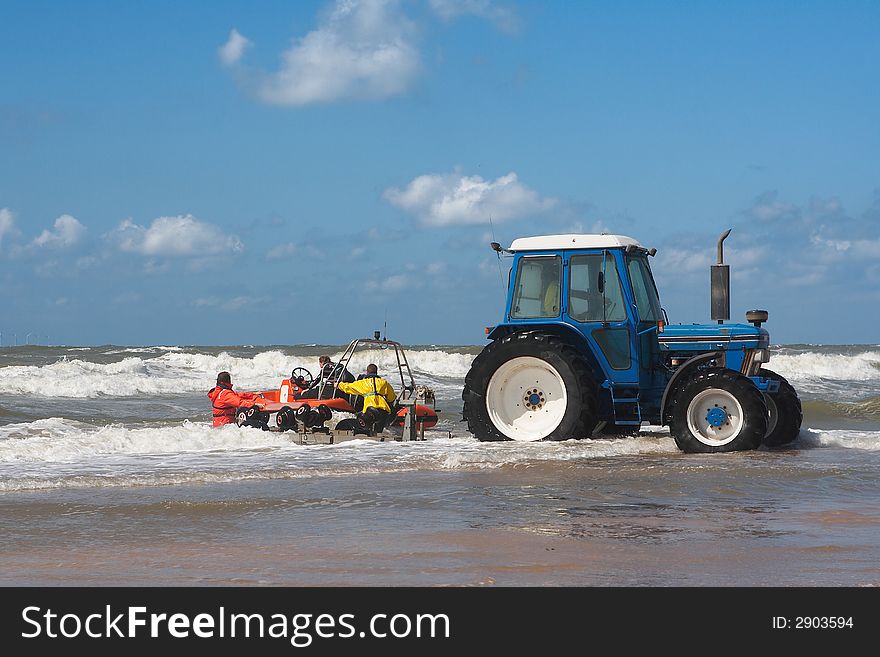 Action shot of a blue tractor in sea water launching a sea rescue raft with 3 people. Hi waves, blue sky with some clouds. Action shot of a blue tractor in sea water launching a sea rescue raft with 3 people. Hi waves, blue sky with some clouds