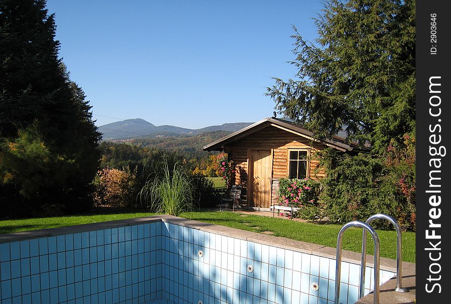 Spring landscape of a garden with an empty swimming pool and a wooden cottage