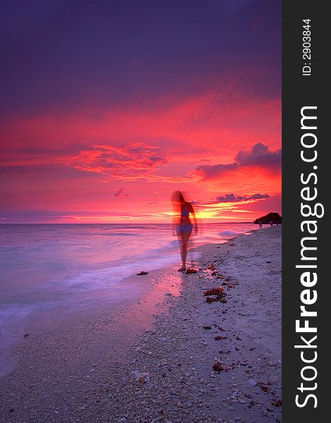 An attractive single woman walking on a beautiful tropical paradise beach at sunset beside a calm sea while on a relaxing vacation. An attractive single woman walking on a beautiful tropical paradise beach at sunset beside a calm sea while on a relaxing vacation