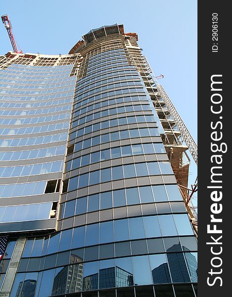 A modern glass skyscraper under construction with a reflection. A modern glass skyscraper under construction with a reflection