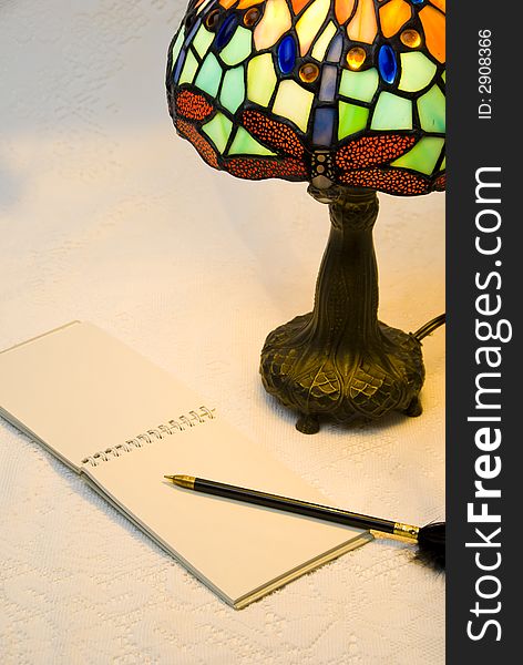 Vertical view of lit stained glass style lamp with open notepad and black pen. Vertical view of lit stained glass style lamp with open notepad and black pen
