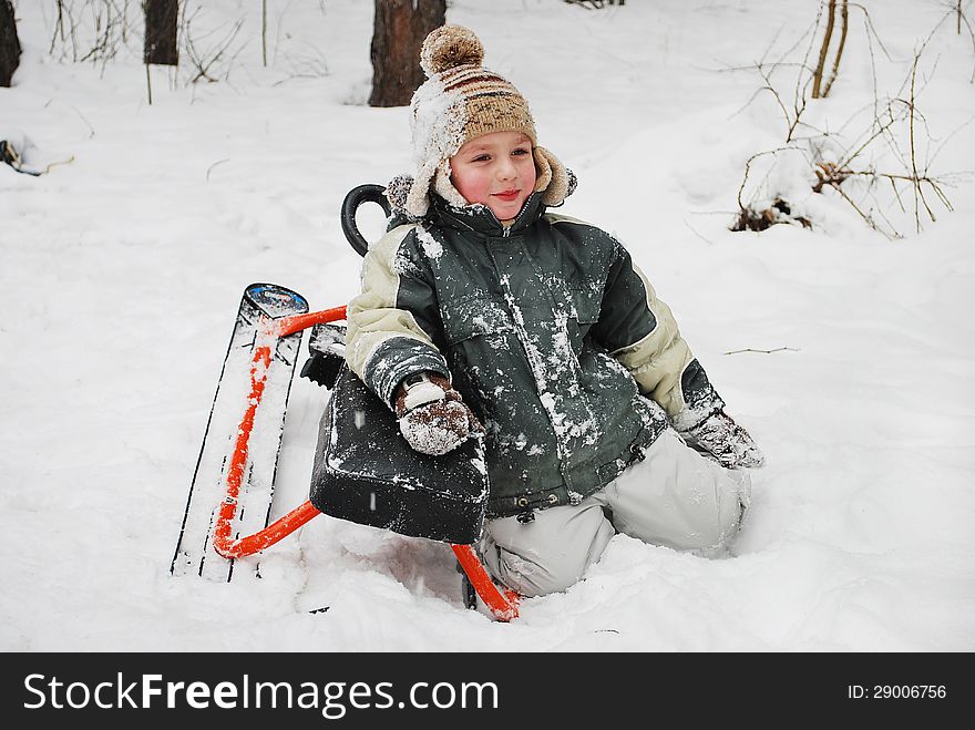 Boy sitting in the snow with sledges.