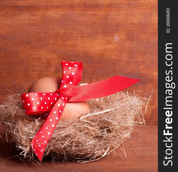 Easter egg in the nest with a red ribbon on the wooden background
