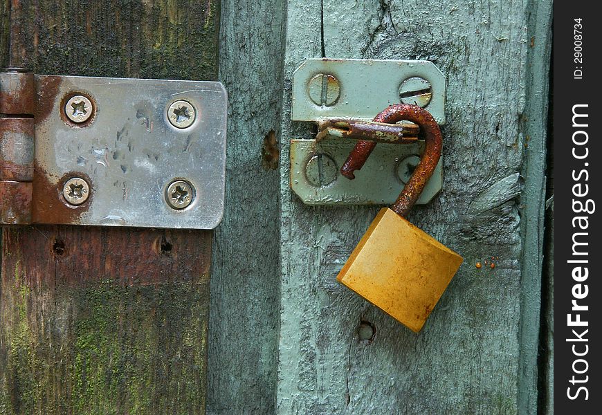 A rusty brass lock hangs on a steel hasp on a green door. A rusty brass lock hangs on a steel hasp on a green door