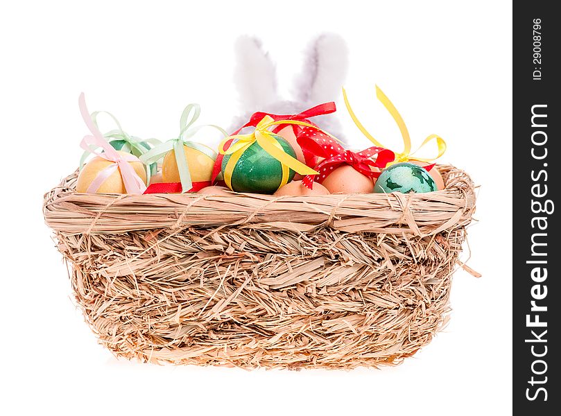 Rabbit looks out of the straw basket with Easter eggs on the white. Rabbit looks out of the straw basket with Easter eggs on the white